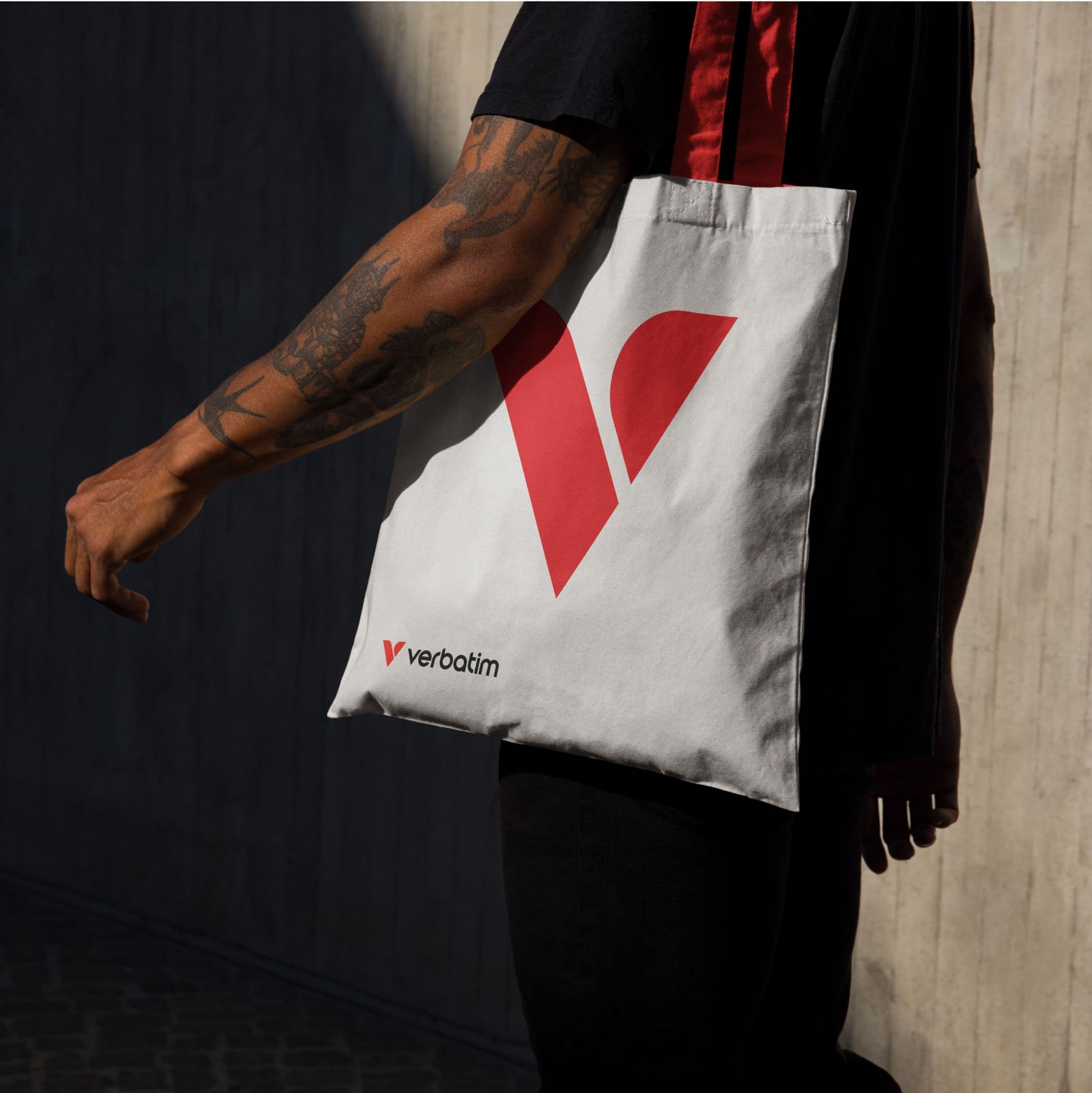 Person holding a white tote bag with a red Verbatim logo.
