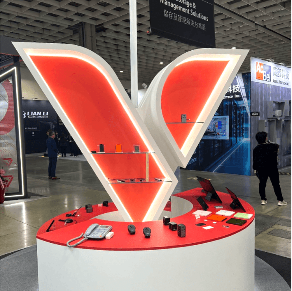 Exhibition booth featuring a large illuminated V design with various tech products displayed.
